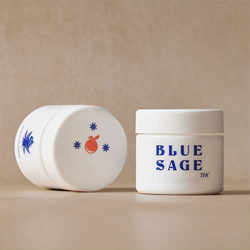 Two white opaque jars of Blue Sage THC product on a neutral background, with one upright showing the blue "BLUE SAGE THC" text logo and the other resting on its side showing an orange fruit and star graphic on its cap.