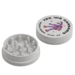 A two-piece speckled gray hemp plastic herb grinder showing the inside teeth base and the top lid printed with a purple astronaut and the text "YES WE CANNABIS," "SESPE CREEK," and "OJAI, CA."